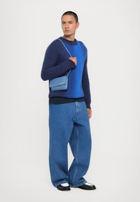 Blå gradientstickad tröja, oversized blå denimbyxor och en liten blå axelväska. Svarta skor med vita detaljer.