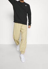 Svart sweatshirt med ribbad mudd, matchad med beige cargo-byxor med avsmalnande ben och vita randiga detaljer på sidorna. Vita sneakers.
