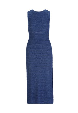 Žena v modrých pletených midi šatách bez rukávov, so zlatým retiazkym náhrdelníkom, zlatým náramkom a hodinkami, drží zlaté listové kabelku, stojí na bielom pozadí.