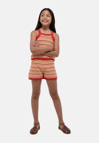 Rompers en tricot jaune et rouge à rayures, avec des bords festonnés et un design de cou Halter. Assorti avec des sandales à lanières marron.