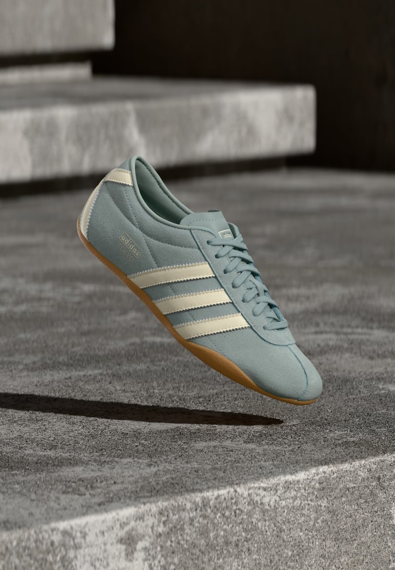 Αθλητικό παπούτσι ανοιχτού μπλε χρώματος με λευκές ρίγες, κατασκευασμένο από μαλακό υλικό, με υφή στην επιφάνεια και καφέ λαστιχένια σόλα.