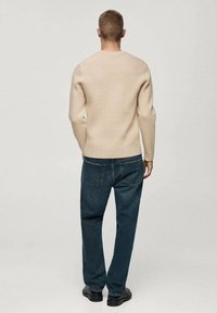 Pull beige en maille avec un col rond, associé à un jean en denim bleu foncé. La tenue présente une finition texturée et une coupe standard.