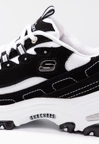 Svart och vit sneaker i mocka och mesh, med en tjock vit sula, silveraccenter och S-logotyp på sidan.