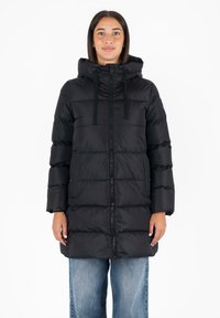 Giubbotto imbottito nero con cappuccio, caratterizzato da una chiusura a zip frontale, tasche sui lati e un motivo rettangolare cucito. Indossato sopra jeans blu a vestibilità ampia.