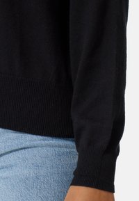 Schwarzer, gestrickter Pullover mit geripptem Muster an den Ärmelbündchen und dem Saum, mit einem lässigen Schnitt und langen Ärmeln. Kombiniert mit hellblauer Denim.