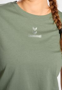 T-shirt in cotone verde oliva con scollatura rotonda, caratterizzato da logo riflettente e design a zigzag in argento sul davanti. Texture morbida.