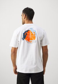 Hvit bomull t-skjorte med et flerfarget grafikk av hender rundt en basketball på baksiden. Korte ermer og en klassisk passform.