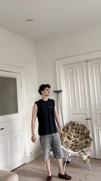 Must have tumes shirt, hallhalli denim lühikesed püksid, pruunid jalanõud. Heledast puidust põrand, valged seinad ja mustriga tool.