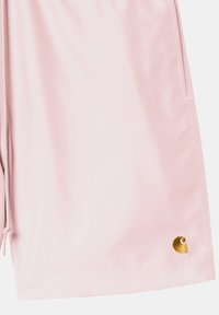 Los pantalones cortos rosa, confeccionados con una tela suave, presentan un bolsillo lateral y un detalle del logo dorado en el dobladillo, con costuras blancas en contraste.