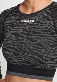 Närbild av en svart och gråmönstrad atletisk crop-top med en Hummel-logotyp, som visar en figurnära design lämplig för sport.
