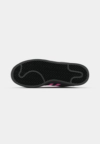 Semelle de chaussure en caoutchouc noir avec des accents rayés roses et un motif en chevrons texturé, dotée d'un bout arrondi et d'un talon courbé.