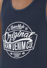 Navy blå top af bomuld med et hvidt logo med teksten: "Union Made," "Original Raw Denim Co.," og "Premium Goods."