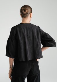 Czarny, fakturowany top z bufiastymi rękawami i zaokrąglonym dekoltem, zestawiony z czarnymi sztruksowymi spodniami; casualowy i luźny krój.