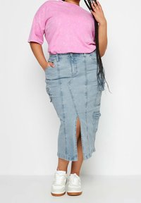 Ljusblå denim midi-kjol med framficka, detalj i fickor och en åtsittande design, matchad med en rosa kortärmad skjorta och vita sneakers.