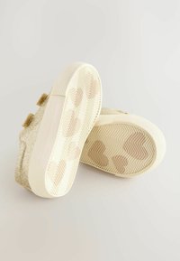 Baskets dorées scintillantes avec une surface texturée, semelles en caoutchouc blanc présentant un motif en chevrons et deux sangles décoratives en velcro.