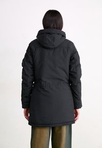 Svart isolerad jacka med huva, med en figurnära midja, långa ärmar och sidofickor, visad bakifrån med en slät yta.