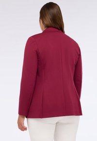 Burgundský blejzr s úzkým střihem, zapínáním na jeden knoflík, klopovými límci a dvěma zadními rozparky, v kombinaci s bílými kalhotami. Hladká textura látky.