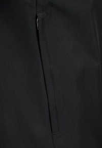 Tela negra con textura suave, que presenta un bolsillo con cremallera y costuras precisas. Diseño minimalista con una apariencia ajustada.