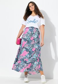 T-shirt blanc avec le texte "Smile" en paillettes bleues, associé à une longue jupe maxi à motifs multicolores dans des tons de rose, bleu et vert, et des baskets blanches.