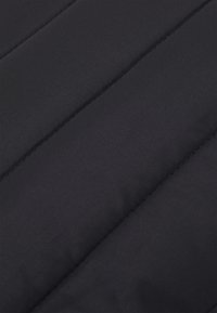 Tissu de veste matelassée noire avec une texture lisse, présentant des coutures diagonales et une isolation pour plus de chaleur. Matériau léger et résistant à l'eau.