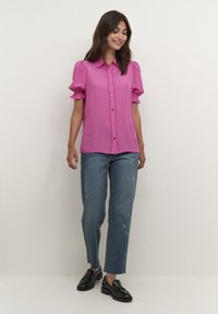 Fuchsia button-up shirt with short puff sleeves, textured fabric, and a straight fit, paired with light-wash jeans and black loafers.