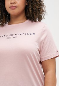 Ružový bavlnený tričko s námorníckou logom "TOMMY HILFIGER EST. 1985" na prednej strane a malou značkovou nášivkou na rukáve. Krátke rukávy, okrúhly dekolt.