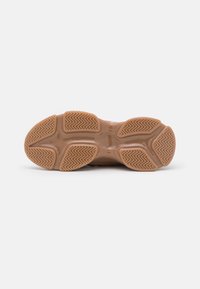 Semelle d'une chaussure en caoutchouc marron avec des motifs de grip texturés et des rainures pour la traction, présentée sur fond blanc uni.
