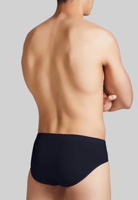 Slip da nuoto neri su un torso nudo, che mostrano un design elegante e minimalista con una texture liscia e una vita media.