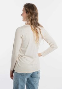 Beige lange mouwen top gemaakt van zacht materiaal, met een ronde hals en een ontspannen pasvorm, gecombineerd met lichtblauwe, losse spijkerbroeken.