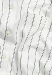 Witte overhemd met verticale blauwe strepen, voorzien van een borstzak, een gladde textuur en ronde, doorschijnende knopen.