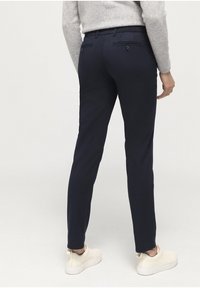 Marinblå byxor med smal passform, som har två bakfickor och bälteshällor. Slät tyg och tapered ben-design. Bärs med beige skor.