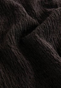 Țesătură neagră texturată cu un model ondulat și ridicat. Suprafețe moi și ușor creponate, prezentând un design complex în nuanțe închise.