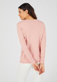 Maglione rosa chiaro realizzato in morbido tessuto a maglia, con maniche lunghe e scollo rotondo, mostrato da dietro con pantaloni bianchi.