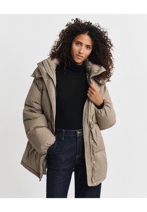 Beige pufferjack met een hoge kraag, drukkers en zijzakken, gecombineerd met een zwarte turtleneck en donkerdenim broek.