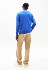 Maglione a maglia blu con texture e colletto rotondo, abbinato a pantaloni di velluto a coste beige e scarpe da ginnastica bianche, visto da dietro.