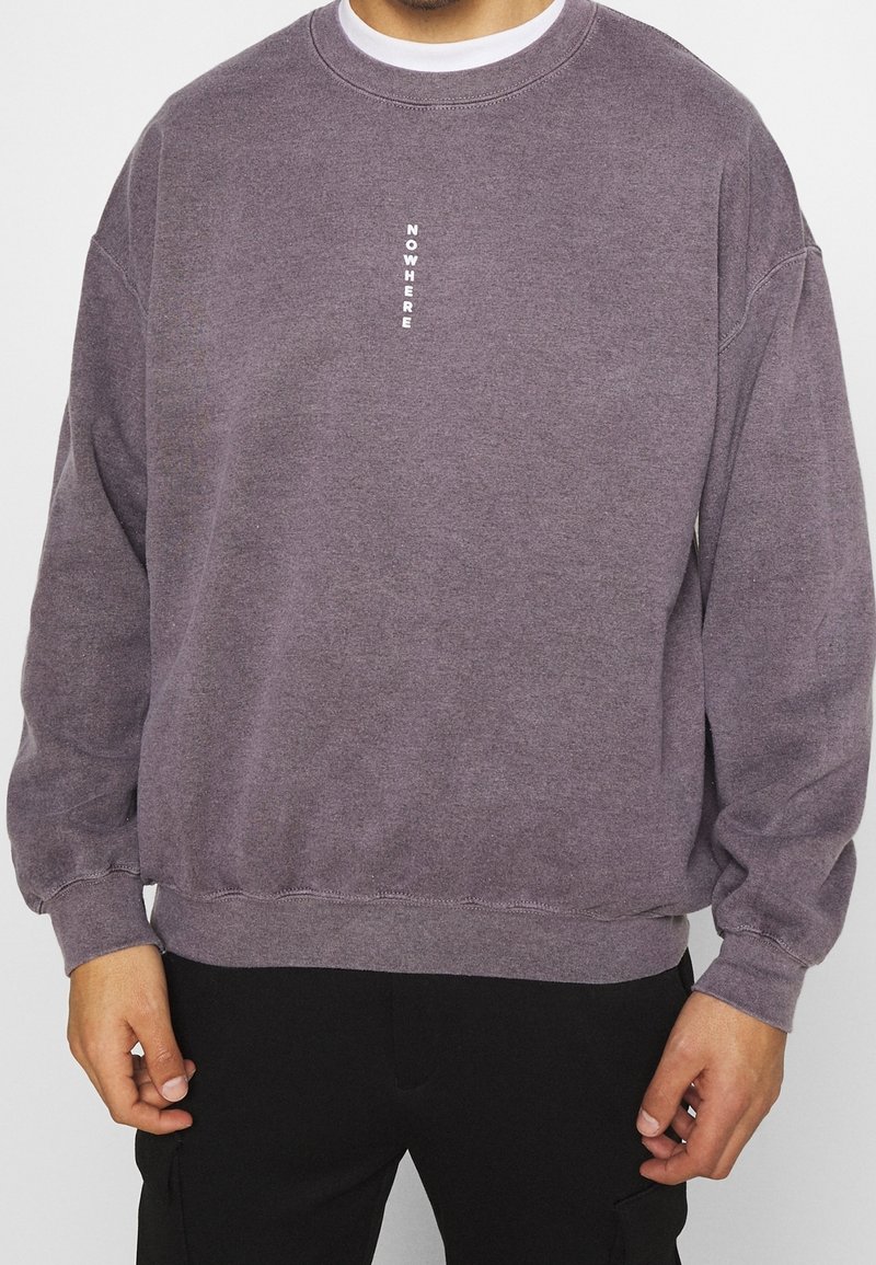 Felpa in cotone lilla chiaro, con scollo rotondo e spalle scese. La scritta "NOWHERE" è stampata verticalmente in bianco sul petto.