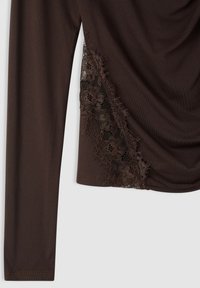 Top marrone a maniche lunghe con design drappeggiato e dettagli in pizzo sul lato, che combina tessuto testurizzato con motivi floreali.