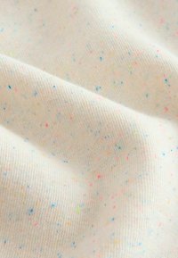 Tessuto di cotone di colore crema con molteplici macchie di rosa, blu e verde. Superficie texture con una sensazione morbida e leggermente elasticizzata.