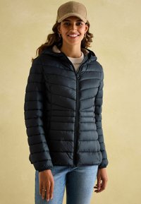 Juodas pūkinis švarkas su kapišonu, užtrauktuku ir horizontaliu siuvinėjimu. Dėvimas virš bežinio megztinio, derinamas su mėlynomis džinsomis.