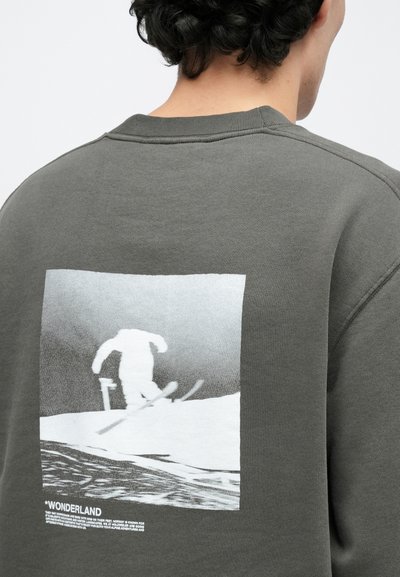 Γκρι βαμβακερό φούτερ με μεγάλο μονόχρωμο γραφικό ενός σκιέρ στην πλάτη, με κείμενο κάτω από την εικόνα σε αντίθετο χρώμα.