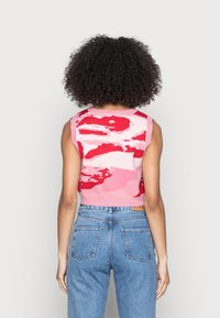 Haut court sans manches en maille avec un motif abstrait rose et rouge. Associé à un jean en denim bleu taille haute, présentant une coupe décontractée.