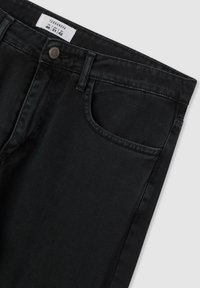 Jeans in denim nero con una vestibilità slim, dotati di cinque tasche, un bottone in metallo e cuciture a contrasto. Etichetta visibile con informazioni sulla taglia.