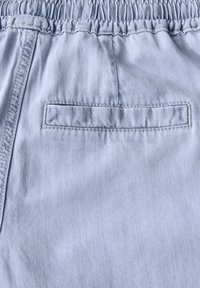 Pantalones cortos de tela azul claro con una cinturilla elástica y un único bolsillo trasero tipo parche, que cuentan con una textura suave y lisa.