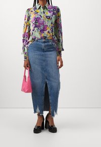 Blouse à fleurs en vert, violet et jaune, associée à une jupe en denim taille haute avec une fente à l'avant et un ourlet effiloché. Sac à main rose et chaussures à plateforme noires.