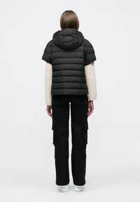 Fekete pehelydzseki kapucnival, rövid ujjakkal és steppelt mintával. Fekete cargo nadrággal és fehér cipővel párosítva.