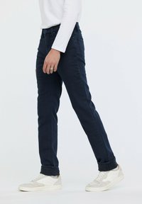Jeans de corte slim en azul marino, confeccionados en denim con una textura suave, que presentan un clásico diseño de cinco bolsillos y puños enrollados, combinados con zapatillas blancas.