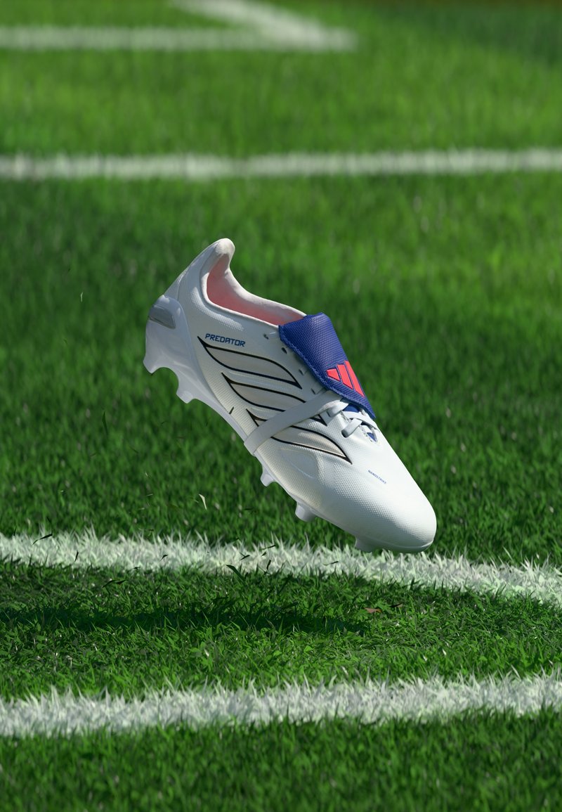 Λευκό ποδοσφαιρικό παπούτσι Adidas Predator με μπλε λεπτομέρεια στην γλώσσα, σε πράσινο χορτάρι κοντά σε λευκές γραμμές του γηπέδου.