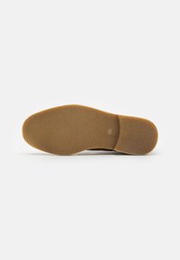Suela de un zapato con una base de goma texturizada de color marrón claro, que presenta una superficie con un patrón diseñado para proporcionar agarre y durabilidad.
