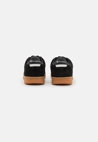 Tenisi negri din suede cu talpă din cauciuc bej, având un tab de călcâi din piele albă și logo-ul Champion pe spate. Design simplu și minimalist.