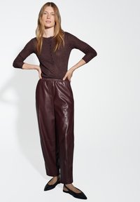 Pantaloni in pelle bordeaux con una vestibilità rilassata, abbinati a un top in maglia scura e scintillante con bottoni e maniche a tre quarti.